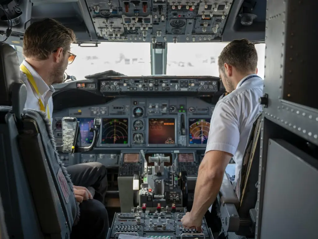 Two pilots navigating an aircraft cockpit, focused on advanced avionics and flight systems.